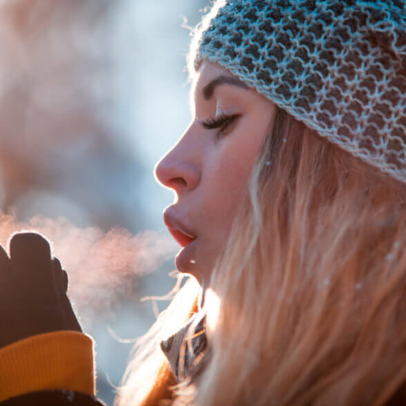 Woman breathing on her hands to keep them warm at cold winter day